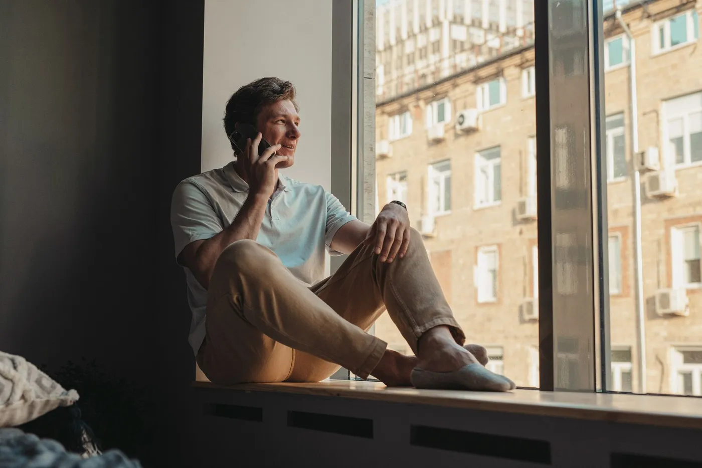 A man sitting by a large window during a phone call