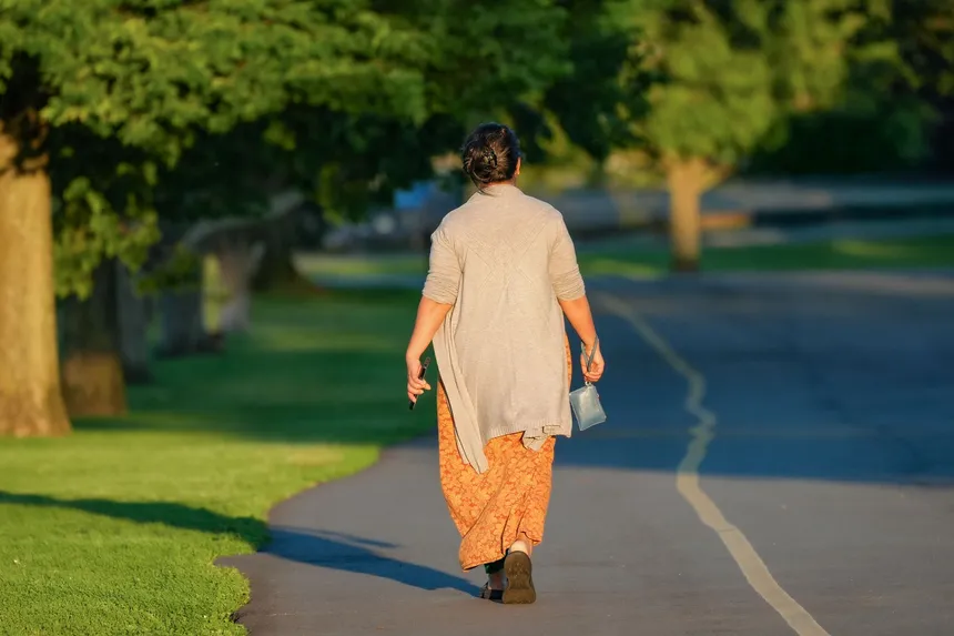 A woman walking along a tree-lined path in morning light